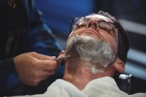 Hombre conseguir barba afeitado con navaja de afeitar en la peluquería - foto de stock