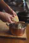 El primer plano de las manos del hombre poniendo rodajas de papa en la olla de guiso en la cocina - foto de stock