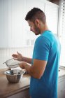 Man sifting flour into a mixing bowl in the kitchen at home — Stock Photo