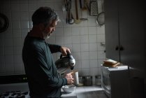 Hombre poring agua caliente del matraz en la cocina - foto de stock