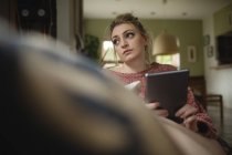 Frau sitzt und nutzt digitales Tablet auf Couch im heimischen Wohnzimmer — Stockfoto