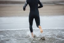 Baixa seção de atleta em terno molhado correndo em direção à praia — Fotografia de Stock