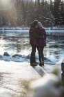 Vista trasera de pareja romántica de pie junto al río en invierno - foto de stock
