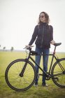 Женщина в солнечных очках держит велосипед в парке — стоковое фото