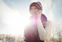Smiling woman in winter wear talking on the phone against bright sunlight — Stock Photo