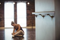 Soporte de barra de ballet en estudio de ballet con mujer atando cordones en el fondo - foto de stock