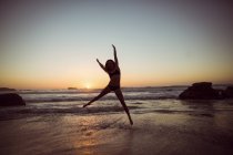 Femme sautant sur la plage pendant le coucher du soleil — Photo de stock