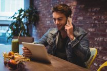 Мужчина разговаривает по мобильному телефону, используя цифровой планшет в кафе — стоковое фото