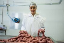 Ritratto di macelleria femminile che tiene salsicce in fabbrica di carne — Foto stock