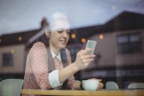 Жінка використовує мобільний телефон, маючи каву в кафе — стокове фото