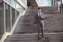 Businessman using mobile phone while walking down steps — Stock Photo