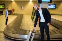 Усміхнений бізнесмен з сумкою на візку в зоні очікування в терміналі аеропорту — стокове фото