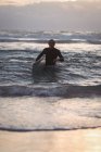 Retrato de un hombre llevando tabla de surf saliendo del mar al atardecer - foto de stock