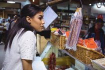 Задумчивый женский персонал, стоящий у стойки для мяса в супермаркете — стоковое фото