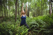 Femme effectuant du yoga en forêt par une journée ensoleillée — Photo de stock