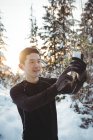 Улыбающийся мужчина зимой делает селфи на мобильном телефоне — стоковое фото
