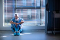 Напружена медсестра чоловічої статі сидить в коридорі лікарні — стокове фото
