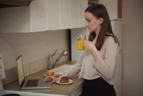 Жінка використовує ноутбук під час сніданку на кухні вдома — стокове фото