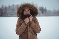Retrato de mujer sonriente con chaqueta de piel disfrutando de la nevada durante el invierno - foto de stock
