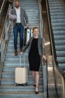 Business people with luggage walking downstairs beside escalator at airport terminal — Stock Photo