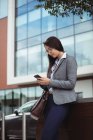 Businesswoman text messaging on mobile phone while standing at city street — Stock Photo