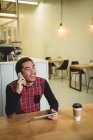 Мужчина разговаривает по мобильному телефону во время использования цифрового планшета в кафе — стоковое фото