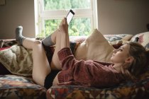 Woman lying and using digital tablet on couch in living room at home — Stock Photo
