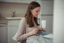 Женщина с цифровым планшетом во время завтрака на кухне дома — стоковое фото
