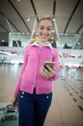 Navetteur féminin avec bagages utilisant un téléphone portable à l'aéroport — Photo de stock