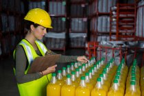 Trabalhadora examinando garrafas de suco na fábrica — Fotografia de Stock