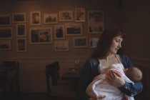 Medio adulto madre sosteniendo lindo bebé en brazos en la cafetería - foto de stock