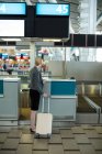 Rear view of businesswoman standing at a check-in counter with luggage in airport terminal — Stock Photo