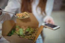Metà sezione della donna utilizzando il telefono cellulare mentre si mangia insalata — Foto stock