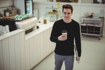 Hombre con portátil sosteniendo una taza de café desechable en la cafetería - foto de stock