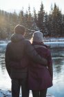 Vista posteriore di coppia romantica in piedi lungo il fiume in inverno — Foto stock