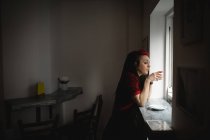 Женщина смотрит в окно, когда пьет кофе в кафе — стоковое фото