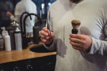Mid section of barber hands holding scissors and shaving brush in barber shop — Stock Photo