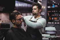 Barber styling client hair in barbershop — Stock Photo