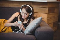 Жінка лежить на дивані, слухаючи музику з мобільним телефоном вдома — стокове фото