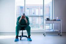 Cirujano tenso sentado en una silla en el pasillo del hospital - foto de stock