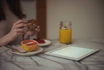 Seção média de mulher desembrulhando cupcake enquanto toma café da manhã em casa — Fotografia de Stock