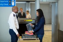 Smiling commuter interacting with airport security officer while collecting accessories from crate in airport — Stock Photo