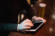 Uomo che utilizza tablet digitale con bicchiere di birra sul bancone nel bar — Foto stock