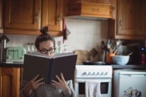 Woman reading book in kitchen at home — Stock Photo