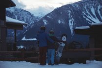 Pareja con snowboard de pie en el campo cubierto de nieve contra las montañas - foto de stock