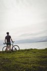 Спортсмен, стоячи з велосипедом на траві на березі моря — стокове фото