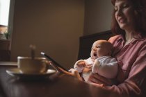 Mãe com bebê usando telefone celular na mesa de café — Fotografia de Stock
