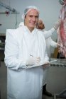 Portrait of male butcher holding clipboard at meat factory — Stock Photo