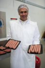 Retrato del carnicero sosteniendo bandejas de embutidos de carne en la fábrica de carne - foto de stock