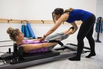 Женщина-тренер помогает женщине с упражнениями на растяжку на реформаторе в тренажерном зале — стоковое фото